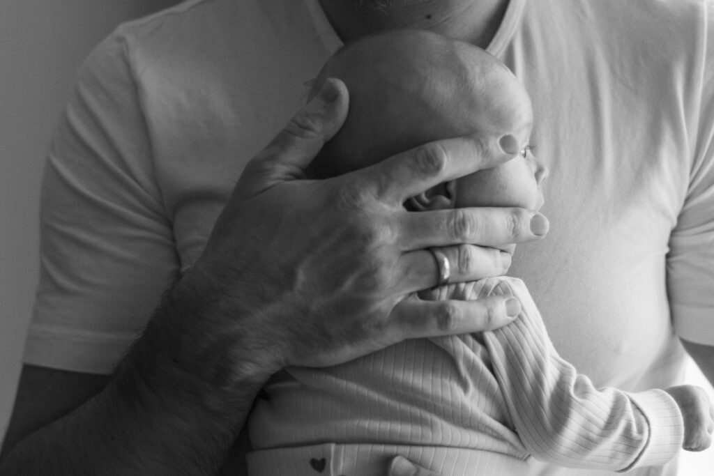 Vater hält Newborn sicher in den Armen – Papa & Baby Fotografie
