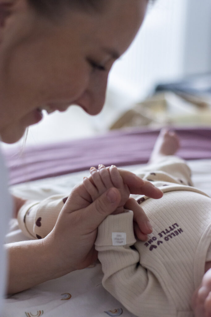 Mutter hält waches Neugeborenes zärtlich an der Hand – Mama & Baby Fotoshooting