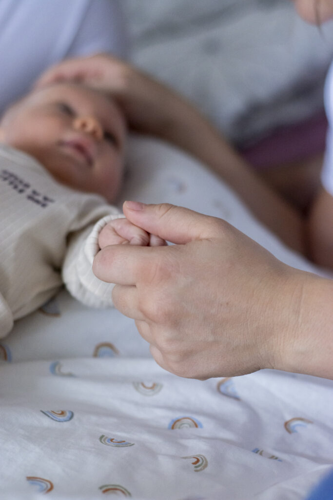 Mutter hält sie anschauende Tochter an der Hand – Babyshooting zu Hause